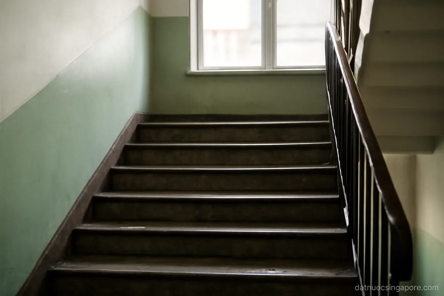 a staircase in a public housing block with worn steps and handrail, natural light from a window